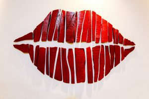 Abstract artwork of red lips created from sliced wood planks on a white background, symbolising the iconic imagery of The Rocky Horror Show.